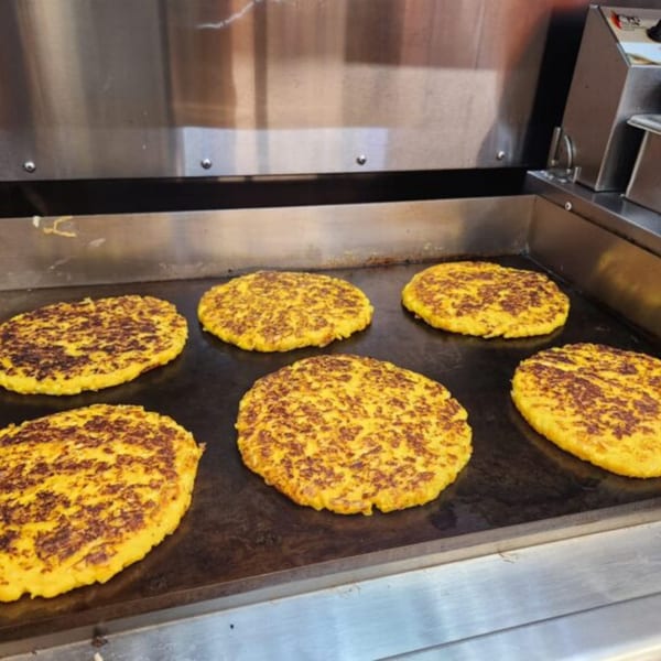 Six golden-brown Venezuelan cachapas cooking on a flat-top grill at Sabrosa Venezuela.
