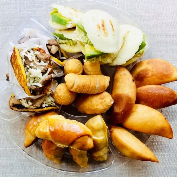 A clear platter filled with various Latin-American appetizers, including arepas, empanadas, and tequeños.