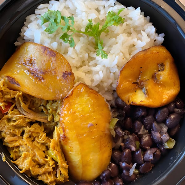 A Latin-American meal with white rice, black beans, shredded chicken, and fried plantains in a black bowl.