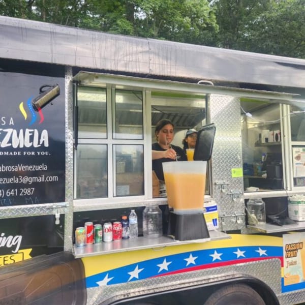 A Sabrosa Venezuela food truck with a worker preparing drinks and a large passion fruit juice dispenser.