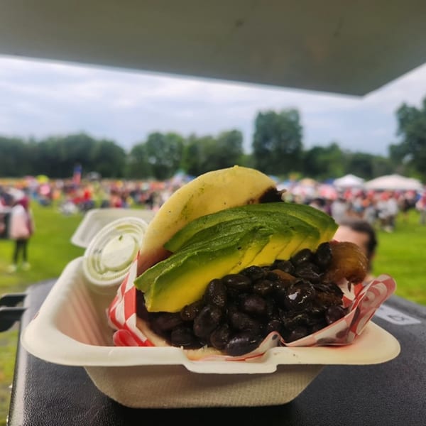 A Sabrosa Venezuela arepa with black beans and avocado, served outdoors at a festival.