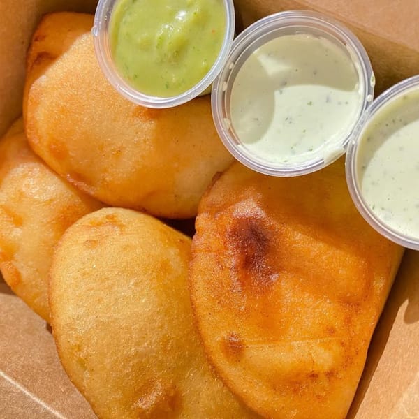Golden-fried Venezuelan empanadas with three small cups of green and white dipping sauces.