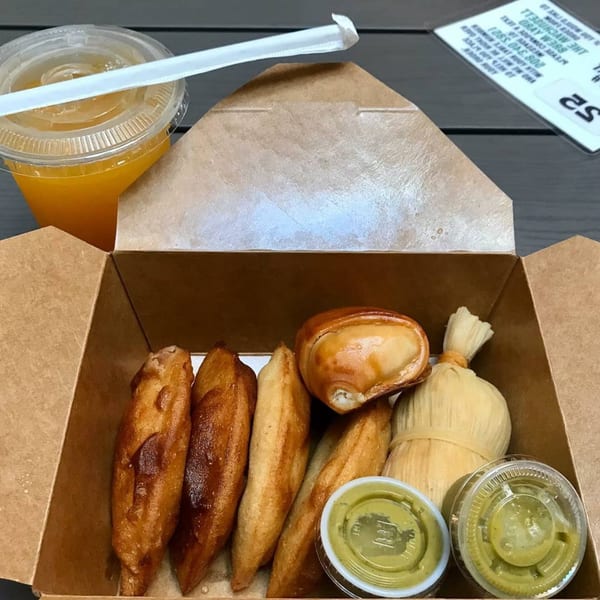 A takeout box of Sabrosa Venezuela empanadas, a tamale, two green sauces, and an orange drink.