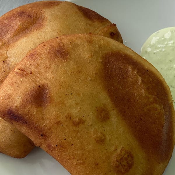 Two golden-brown Sabrosa Venezuela empanadas with a side of light green sauce on a white plate.