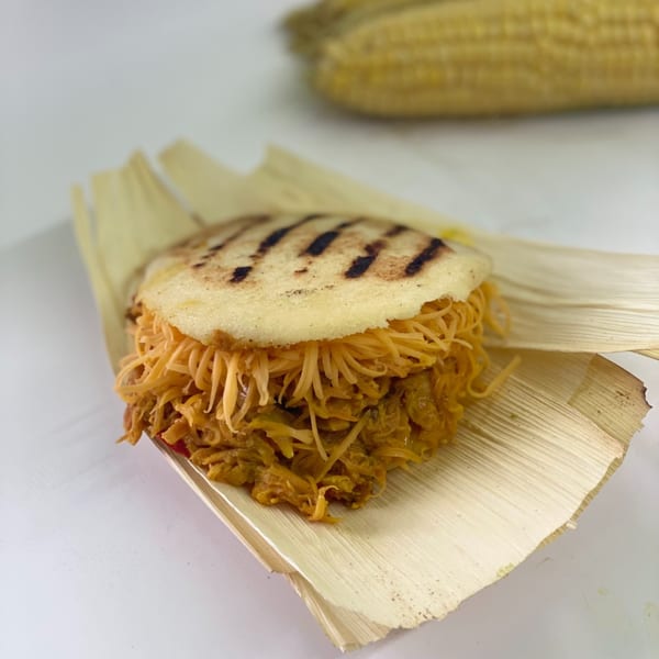 A Sabrosa Venezuela arepa filled with shredded meat and cheese, served on a corn husk.
